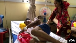 Boeun Bol, a victim of a traffic accident, rests on a hospital bed while his wife, Ma Phearavy, looks after him in Phnom Penh, Cambodia, May 11, 2020. (Sun Narin/VOA Khmer)