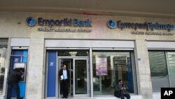 A man (L) makes a transaction at an ATM machine outside an Emporiki Bank branch in Athens, March 9, 2012. 