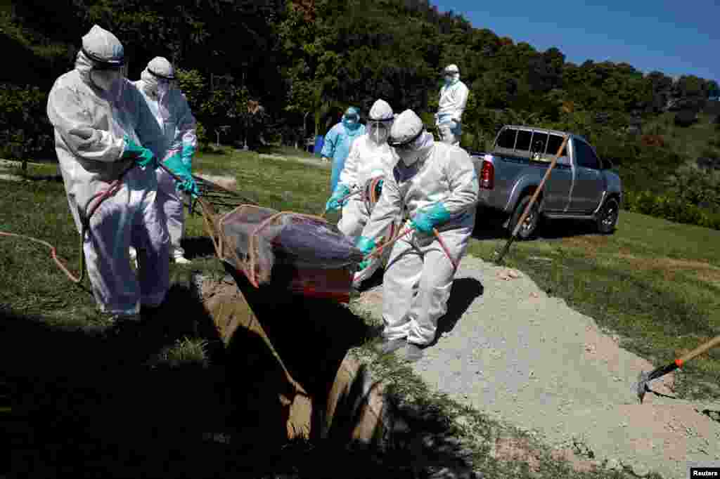 En El Salvador, trabajadores entierran el ataúd de un hombre, que murió de COVID-19, en el Cementerio Jardín, mientras continúa el brote de COVID-19, en Soyapango.