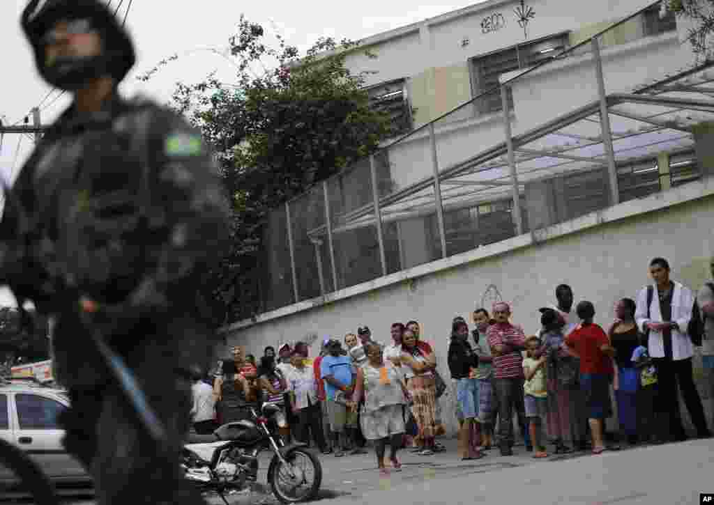 A soldier stands guard where people wait in line to vote in general elections outside a school at the Mare Complex slum in Rio de Janeiro, Brazil, Oct. 26, 2014.