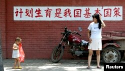 一個媽媽和孩子在“計劃生育是我國基本國策”的標語前走過。（2002年7月23日）