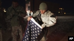 A soldier with the 3rd Brigade Combat Team, 1st Cavalry Division folds up a U.S. flag outside their Mine Resistant Ambush Protected (MRAP) vehicle before leaving Camp Adder near Nasiriyah to travel with the last U.S. military convoy to leave Iraq Sunday, 