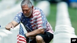 J.D. Madrid toca la lápida de su suegro, Michael McBrien, en el cementerio nacional de Fort Logan, en Sheridan, Colorado. Mayo 23 de 2020.