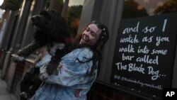 Brodie MacArthur, fan de Taylor Swift, del este de Londres, posa con el perro de un amigo junto a un cartel con letras de Taylor Swift afuera del pub Black Dog en Vauxhall, Londres, el sábado 4 de mayo de 2024.