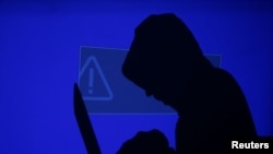 ARSIP - Seorang pria bertudung memegang laptop sementara layar biru dan tanda seru diproyeksikan di belakangnya (Ilustrasi: REUTERS/Kacper Pempel)