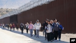 FILE - A group of people, including many from China, walk along the wall after crossing the border with Mexico to seek asylum, near Jacumba, California, Oct. 24, 2023.