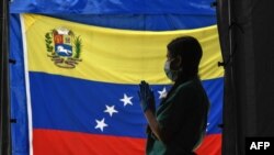 Un miembro del personal de Médicos Sin Fronteras se prepara a la espera de que los pacientes se realicen la prueba de COVID-19 frente a una bandera venezolana en el Hospital Pérez de León del barrio Petare, en Caracas. Junio 23, 2020.