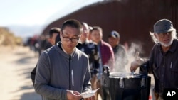 Un migrante chino recibe avena cocida de manos de un voluntario mientras aguarda junto con otras personas para solicitar asilo tras cruzar la frontera con México, el martes 24 de octubre de 2023, cerca de Jacumba, California. 