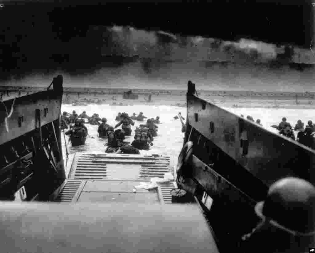 While under heavy machine gun fire from the German coastal defense forces, American soldiers maneuver off the ramp of a U.S. Coast Guard landing craft during the Allied landing operations at Normandy, France, June 6, 1944.