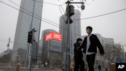 Residents walk past a retail and office district with a screen showing propaganda which reads "Go China! Go Wuhan" as businesses slowly restart in Beijing March 8, 2020.