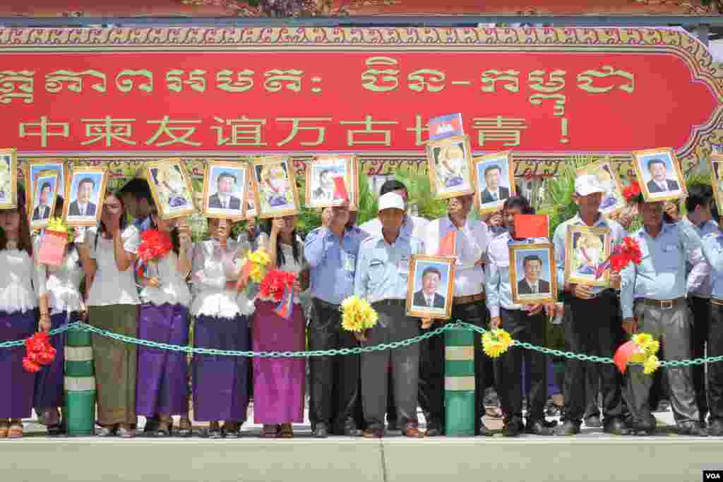ប្រជាពលរដ្ឋកាន់បដារូបប្រធានាធិបតីចិនលោក Xi Jinping និងរូបព្រះមហាក្សត្រកម្ពុជា ព្រះបាទ នរោត្តម សីហមុនី ខណៈពេលរង់ចាំការមកដល់របស់លោកប្រធានាធិបតី នៅក្រុងភ្នំពេញ នាថ្ងៃទី១៣ ខែតុលា ឆ្នាំ២០១៦។ (ឡេង ឡែន/VOA) 