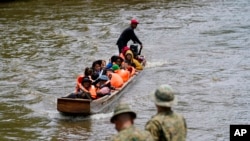 Migrantes que se dirigen al norte llegan a Lajas Blancas, donde un agente de la policía fronteriza panameña se encuentra en la orilla del río Chucunaque, en la provincia de Darién, Panamá, el 6 de octubre de 2023, después de cruzar caminando el Tapón del Darién desde Colombia.