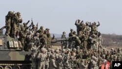 着灰色军装的美军士兵和韩国士兵2012年3月15日在分割朝鲜半岛非军事区以南韩国境内的罗德里格山岭附近举行的年度雏鹰演习期间的一次实弹射击演习之后欢呼
