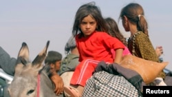 FILE - Displaced children from the minority Yazidi sect, fleeing violence from forces loyal to the Islamic State in Sinjar town, ride on a donkey as they head toward the Syrian border town of Elierbeh, Aug. 11, 2014.