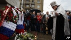 A Russian Orthodox priest prays as Moscovites light candles at a memorial to three men killed in the August 1991 hard line Communist coup attempt during a ceremony marking the 20th anniversary of the failure of the coup in downtown Moscow, Saturday, Aug.