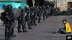 Un manifestante se sienta frente a una escuadrón de policías con equipo antidisturbios durante una protesta contra el gobierno en Bogotá, Colombia, el lunes 21 de septiembre de 2020. 