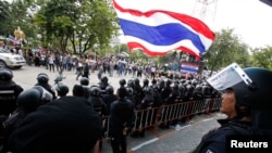 An anti-government protester waves a national flag in front of riot police officers and soldiers guarding the entrance of the National Broadcast Services of Thailand (NBT) television station in Bangkok, May 9, 2014.
