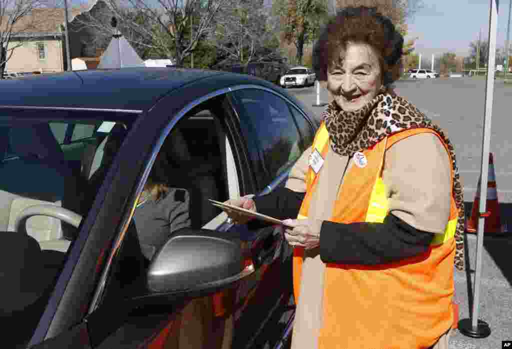 Observatrice des élections, Kathryn Ballen, à droite, vérifie un bulletin de vote qu’elle prend des mains d’un chauffeur qui s’avance pour voter au parking de Harvard Gulch Recreation Center au Denver Sud, vendredi le 31 octobre 2014. (AP Photo / David Zalubowski)