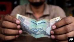 Seorang kasih di sebuah restoran di New Delhi memegang uang kertas rupee (foto: dok).