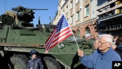 Чоловік тримає прапорець США біля американської броньованої машини Stryker з конвою військ НАТО під час зупинки для зустрічі з місцевими жителями в Білостоку, Польща. 24 березня 2015 р.