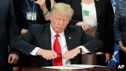 Le président Donald Trump tirant un stylo avant de signer une ordonnance pour des actions d'immigration pour construire du mur lors d'une visite au département de sécurité intérieure à Washington, le mercredi 25 janvier 2017. (AP Photo / Pablo Martinez Monsivais)