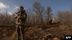 Seorang prajurit Ukraina berjaga-jaga memeriksa adanya drone Rusia di langit sementara seorang prajurit dalam traktor menggali sistem parit di wilayah Zaporizhzhia, 30 Januari 2024. (Foto: AFP)