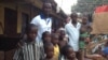 Daddy Hasan Kamara stands outside his Freetown, Sierra Leone, home with family members.
