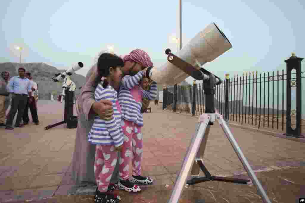 Seorang ayah dan dua putrinya meneropong bulan baru tanda datangnya Ramadan dari teleskop di atas gunung Jebel Hafeet di Al Ain, Uni Emirat Arab (16/6). (AP/Kamran Jebreili)