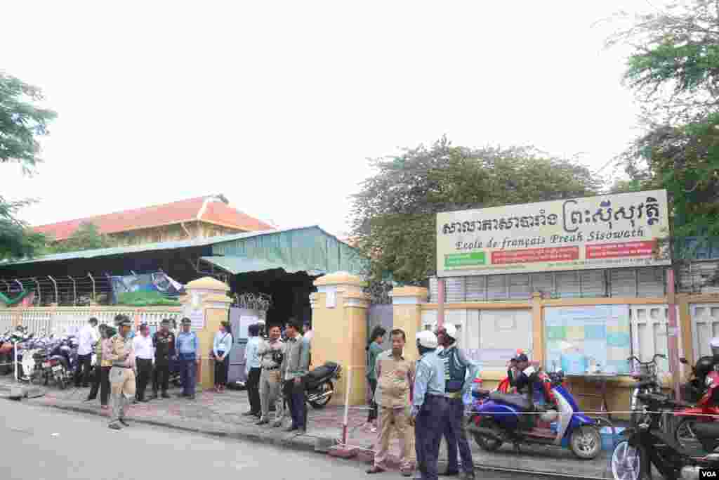 នគរបាលកំពុងឈររក្សាសន្តិសុខ ខណៈអនុរក្សកំពុងឈរចាំត្រួតពិនិត្យបេក្ខជនមុននឹងអនុញ្ញាតឱ្យចូលក្នុងមណ្ឌលប្រលងវិទ្យាល័យព្រះស៊ីសុវត្ថិ កាលពីថ្ងៃទី២៤ សីហា ឆ្នាំ២០១៥។ (ស៊ូ ពិសែន/VOA)