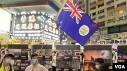 反送中運動6-12一周年十八區街頭展覽，在銅鑼灣展覽場地有人高舉港英殖民時代香港旗幟。