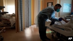 El capellán Elías Mena sostiene la mano de un paciente de COVID-19 mientras ora por él en el Centro Médico Providence Holy Cross, en el sector Mission Hills, de Los Angeles el 15 de enero. 