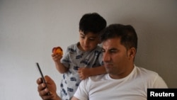 FILE - Special Immigrant Visa Afghan Abdul Aman Sediqi, a U.S. Special Immigrant Visa (SIV) recipient, and his son Elyan watch news from Kabul following their evacuation from Afghanistan in Houston, Texas, Aug 26, 2021.