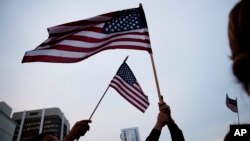Residentes en Orlando ondean banderas estadounidenses durante una vigilia en el centro de la ciudad por las víctimas de la masacre del club nocturno Plulse.