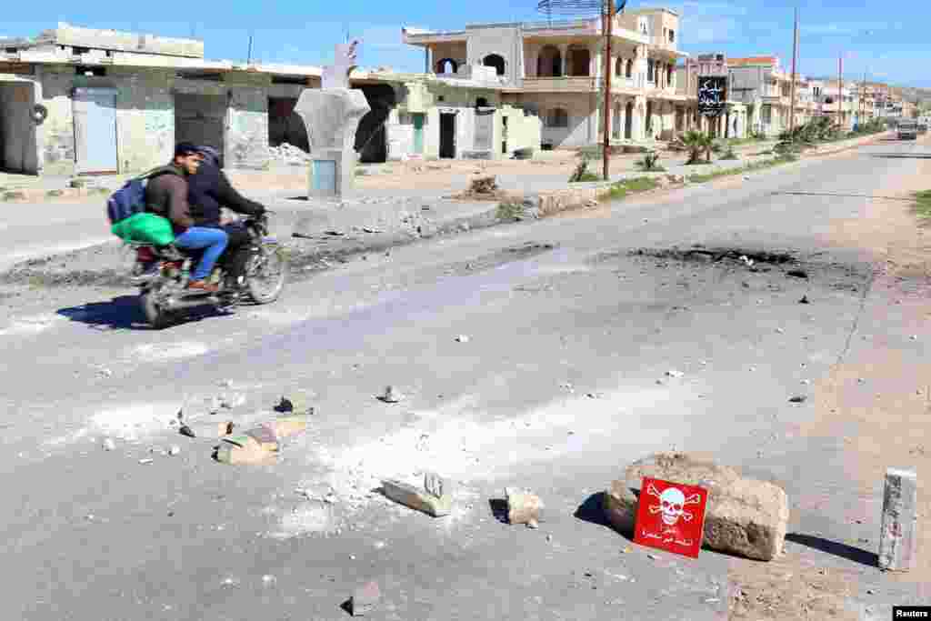 Men ride a motorbike past a hazard sign at a site hit by an airstrike on Tuesday in the town of Khan Sheikhoun, April 5, 2017. The hazard sign reads, "Danger, unexploded ammunition."