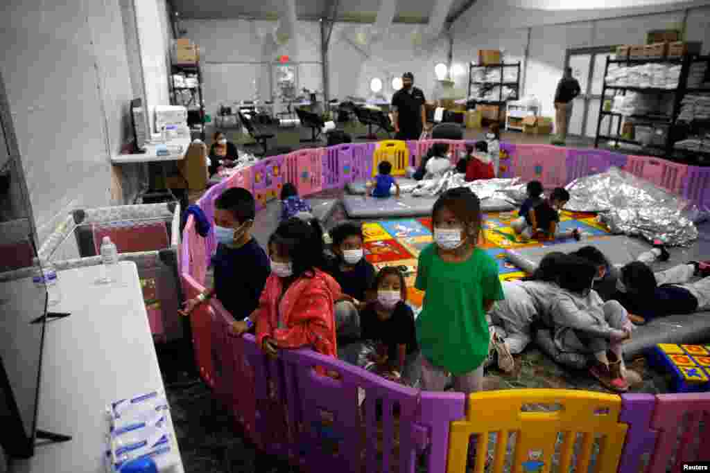 Niños migrantes no acompañados, de 3 a 9 años, ven televisión dentro de un corralito.
