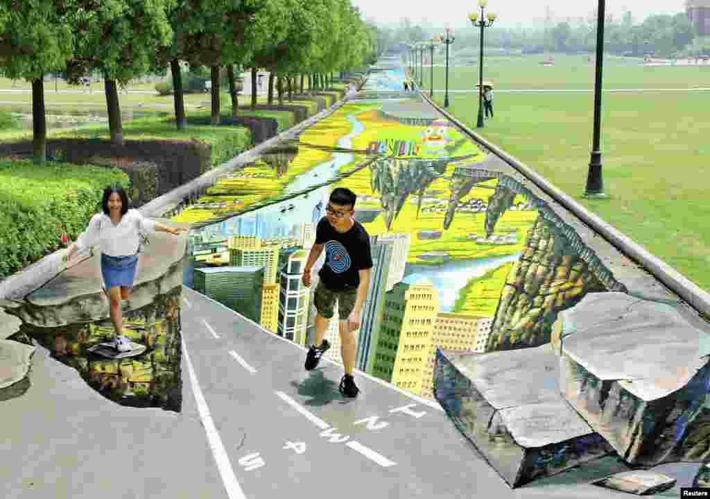Dua mahasiwa berpose di lukisan 3D di dekat kampus mereka di kota Nanjing, Jiangsu, China.