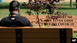 A man sits near a bench memorializing people who died from COVID-19 in Bayonne, N.J., Thursday, May 20, 2021. (AP Photo/Seth Wenig)
