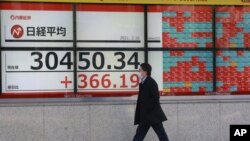 Un hombre que lleva una mascarilla pasa junto al cartel electrónico de una firma de valores en Tokio, el martes 16 de febrero de 2021. 