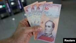 A man shows the new five and ten Bolivar Soberano (Sovereign Bolivar) bills, after he withdrew them from an automated teller machine (ATM) at a Mercantil bank branch in Caracas, Venezuela, Aug. 20, 2018. 