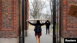 FILE - A student carries a box to her dorm at Harvard University, after the school said it would move to virtual instruction for graduate and undergraduate classes, in Cambridge, Massachusetts, March 10, 2020.