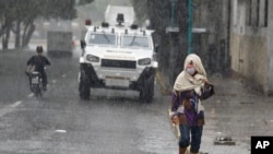 Una mujer camina el 9 de Julio de 2021 bajo la lluvia mientras un vehículo armado transita por las calles cercanas a la Cota 905, en Caracas, Venezuela, una de las comunidades más peligrosas del país suramericano, .