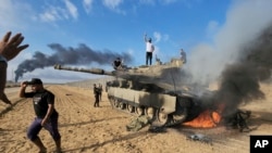 Palestinci slave pored uništenog izraelskog tenka u pojasu Gaze (Foto: AP/Hassan Eslaiah)