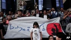 FILE - A girl stands in front of a banner written in Arabic that reads "remove our shackles," during a protest in front of the Press Syndicate in Cairo, Egypt, May 3, 2016.