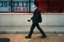 A man wearing a face mask walks past an electronic stock board showing Japan's Nikkei 225 index at a securities firm in Tokyo Monday, May 11, 2020.