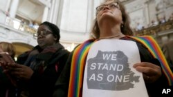 Pastor Annie Steinberg-Behrman (kanan) dari Gereja Metropolitan Community, memegang kertas pernyataan dukungan saat menghadiri rapat di Balai Kota San Francisco untuk menekankan lagi komitmen kota itu sebagai kota perlindungan, November 2016. (AP/Jeff Chiu)