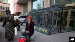 2014年5月1日，一位維吾爾婦女坐在烏魯木齊街頭，身後是鐵籠保護下的中國武警。