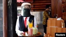 A waiter wearing a face shield and a protective face mask carries a tray with drinks as she serves customers in a Bumi Aki restaurant amid the coronavirus disease (COVID-19) outbreak in Bogor, near Jakarta, Indonesia, May 29, 2020. 