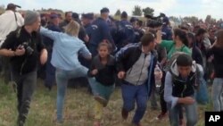 Juru kamera Hungaria Petra Laszlo (kiri tengah, berbaju biru), menendang migran muda yang baru saja menyeberangi perbatasan dari Serbia dekat Roszke, Hungaria (8/9). 