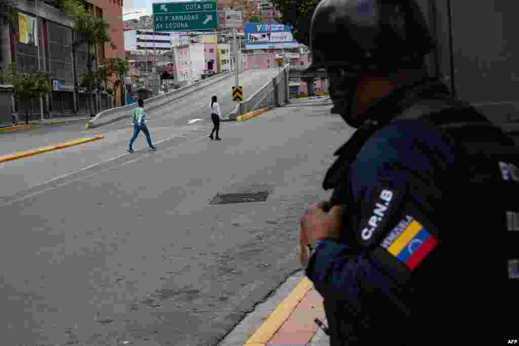 Un miembro de la Policía Nacional Bolivariana observa a dos mujeres cruzar durante enfrentamiento. A pesar de los reportes extraoficial, todavía no hay información oficial de víctimas o heridos por la situación. Junio, 8 2021. Foto: Yuri Cortez - AFP.