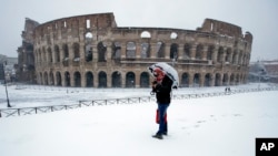 A man stands in front of the ancient Colosseum blanketed by the snow in Rome, Feb. 26, 2018. (AP Photo/Alessandra Tarantino)